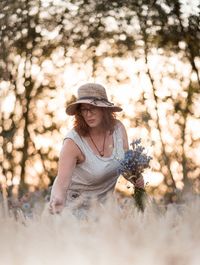 Mature woman holding flower between cereal plants looking away