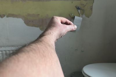 Optical illusion of man hand holding toilet paper in bathroom against wall