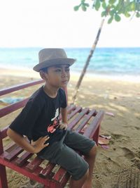 Boy sitting on beach by sea