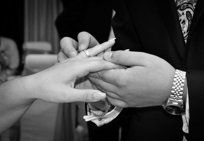 Midsection of groom wearing ring to bride in wedding ceremony