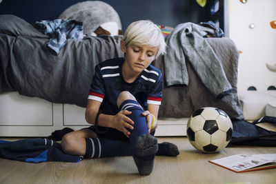 Blond boy wearing sock while sitting in bedroom at home