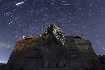 Low angle view of statue against star trail