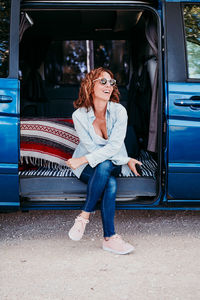 Woman wearing sunglasses holding mobile phone while sitting in camper trailer