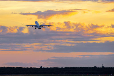 Low angle view of airplane flying in sky at sunset