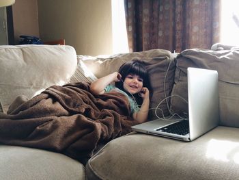 Cute girl listening music from laptop while lying on sofa at home