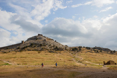 People on field by mountain against sky