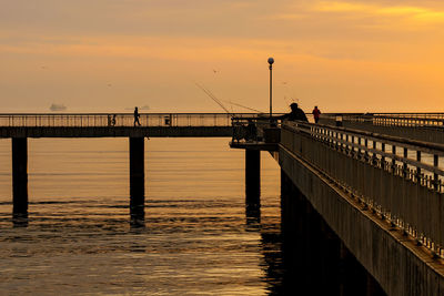 Silhouette fishing pier on sea against sky during sunset