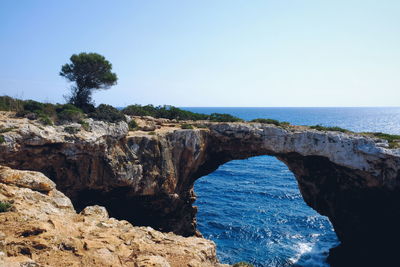 Rock formations by sea against clear blue sky