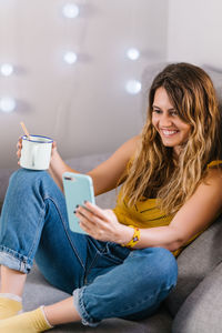 Young woman using mobile phone while sitting on sofa