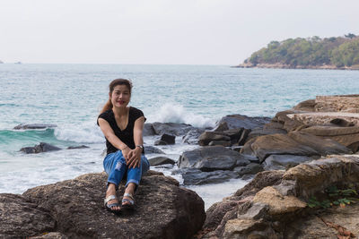 Full length portrait of woman sitting on rock at beach