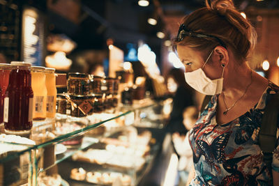 Young woman shopping in grocery store in the evening, wearing the face mask to avoid virus infection