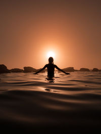 Silhouette woman standing in sea against sky during sunset