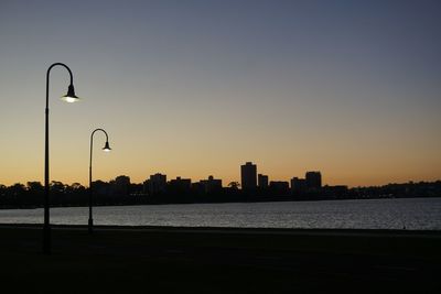 Silhouette city by sea against sky during sunset