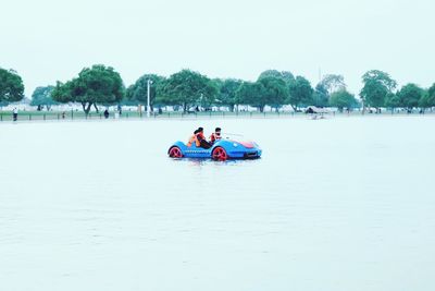 People on boat in lake against clear sky