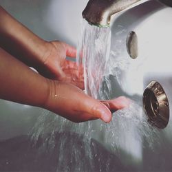 Water from faucet falling on cropped hands in bathtub