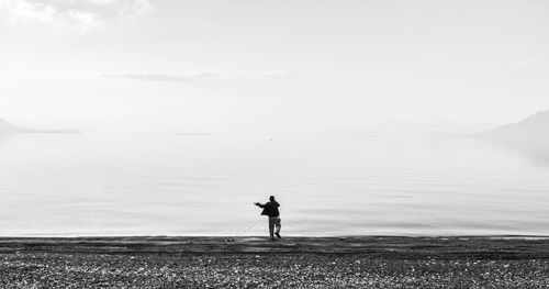 Full length of man throwing rock in sea against sky