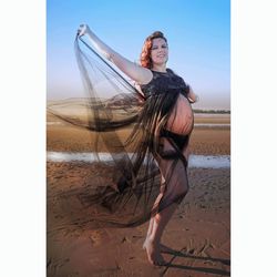 Pregnant woman standing at beach against sky during sunset