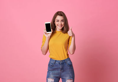 Portrait of smiling young woman photographing against pink background