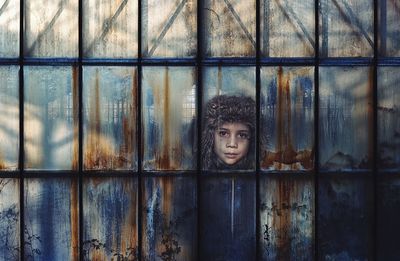 Portrait of boy seen through damaged window of building