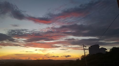 Low angle view of silhouette electricity pylon against dramatic sky