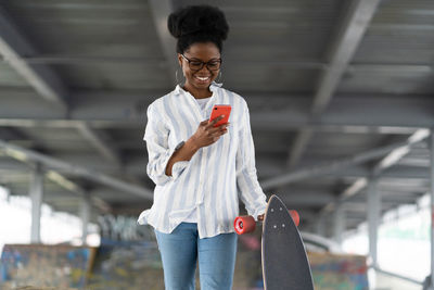 Smiling woman using mobile phone with skateboard