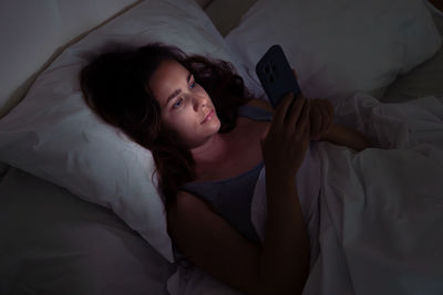 Young woman using mobile phone while lying on bed at home