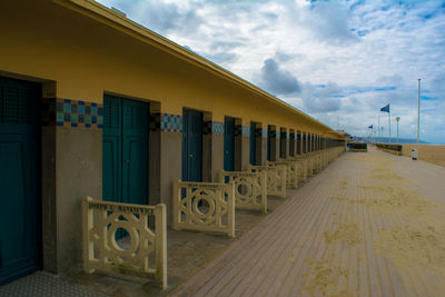 Walkway by building against cloudy sky