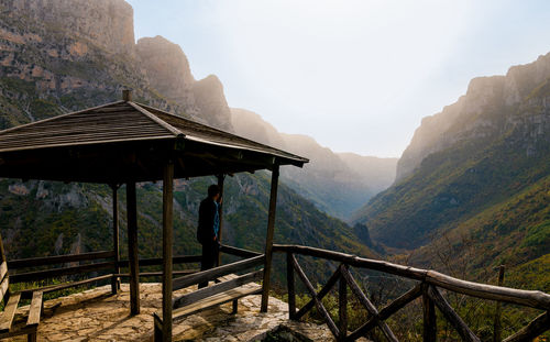 Side view of man looking at mountains from gazebo against sky