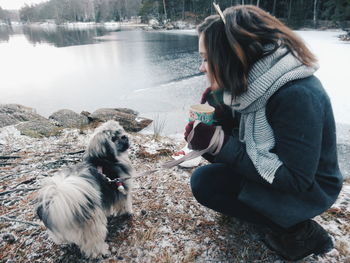 Woman with puppy crouching at lakeshore during winter