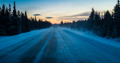 Snow covered road against sky at sunset