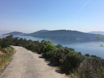 Road by sea against clear blue sky