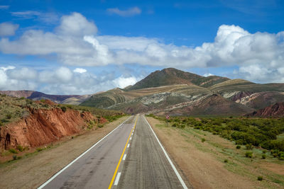 Road leading towards mountains against sky