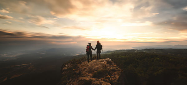 Rear view of man standing on mountain against sky during sunset