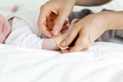 Cropped hands of woman applying bandage to baby sleeping on bed