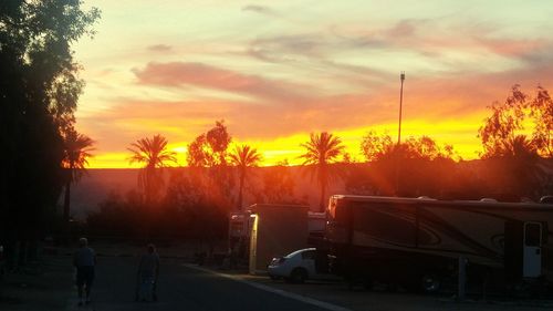 Road by silhouette trees against orange sky