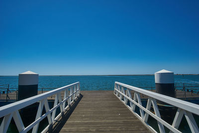 Pier on sea against clear blue sky