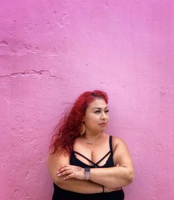 Young woman standing against pink wall