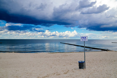 Signboard by garbage can at beach with baltic sea against cloudy sky