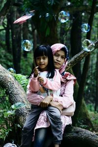 Portrait of mother and daughter by bubbles in forest