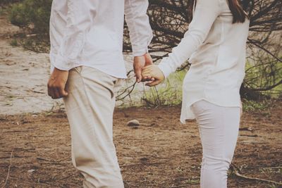 Midsection of couple holding hands while standing on field 