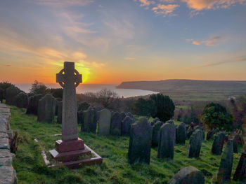 Cross at cemetery against sky during sunset