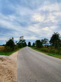Empty road along plants and trees against sky