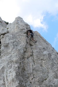 Low angle view of person climbing rocky mountain against sky