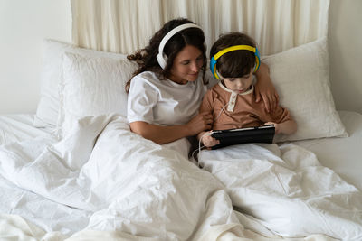 Family morning in bedroom. mom in headphones look at little kid son play games on tablet computer