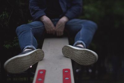 Close-up of man sitting on seesaw at park