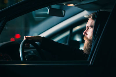 Bearded young man sitting in car seen through window at night