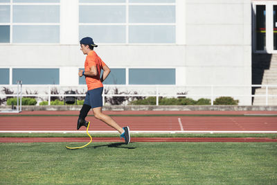 Side view of athlete with prosthetic leg running on grass at track