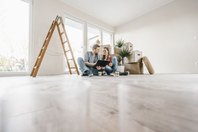 Couple sitting on floor of their new home among moving boxes