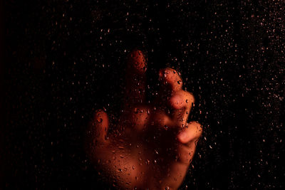 Cropped hands of person seen through wet glass