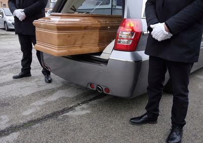Low section of men standing amidst casket in van on road